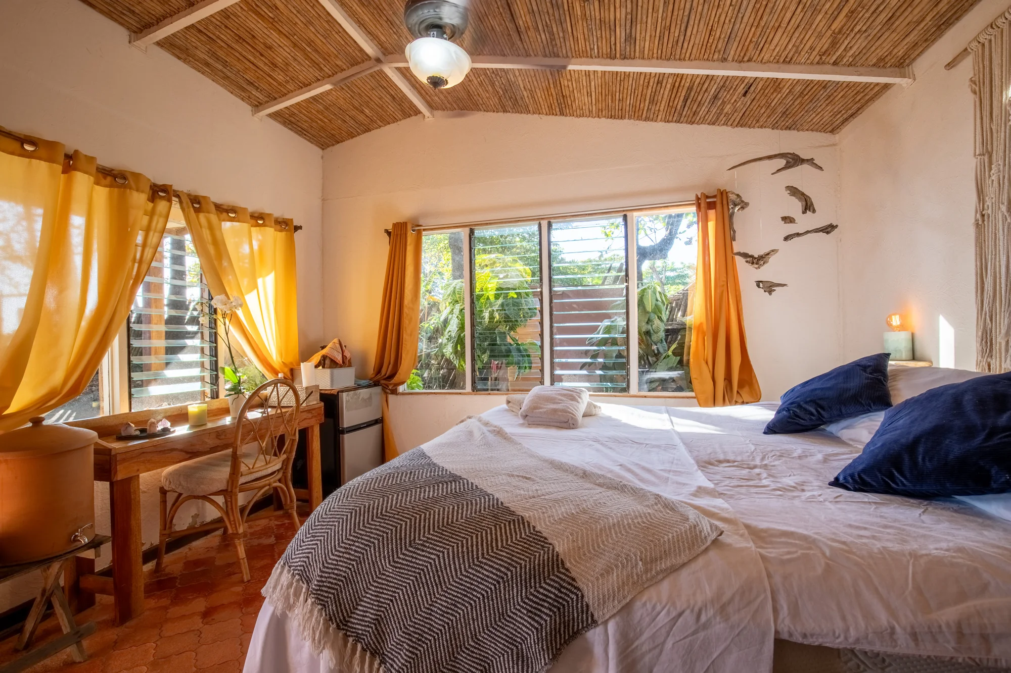 Beachfront Cabina bedroom with blue cushions, yellow curtains and a desk