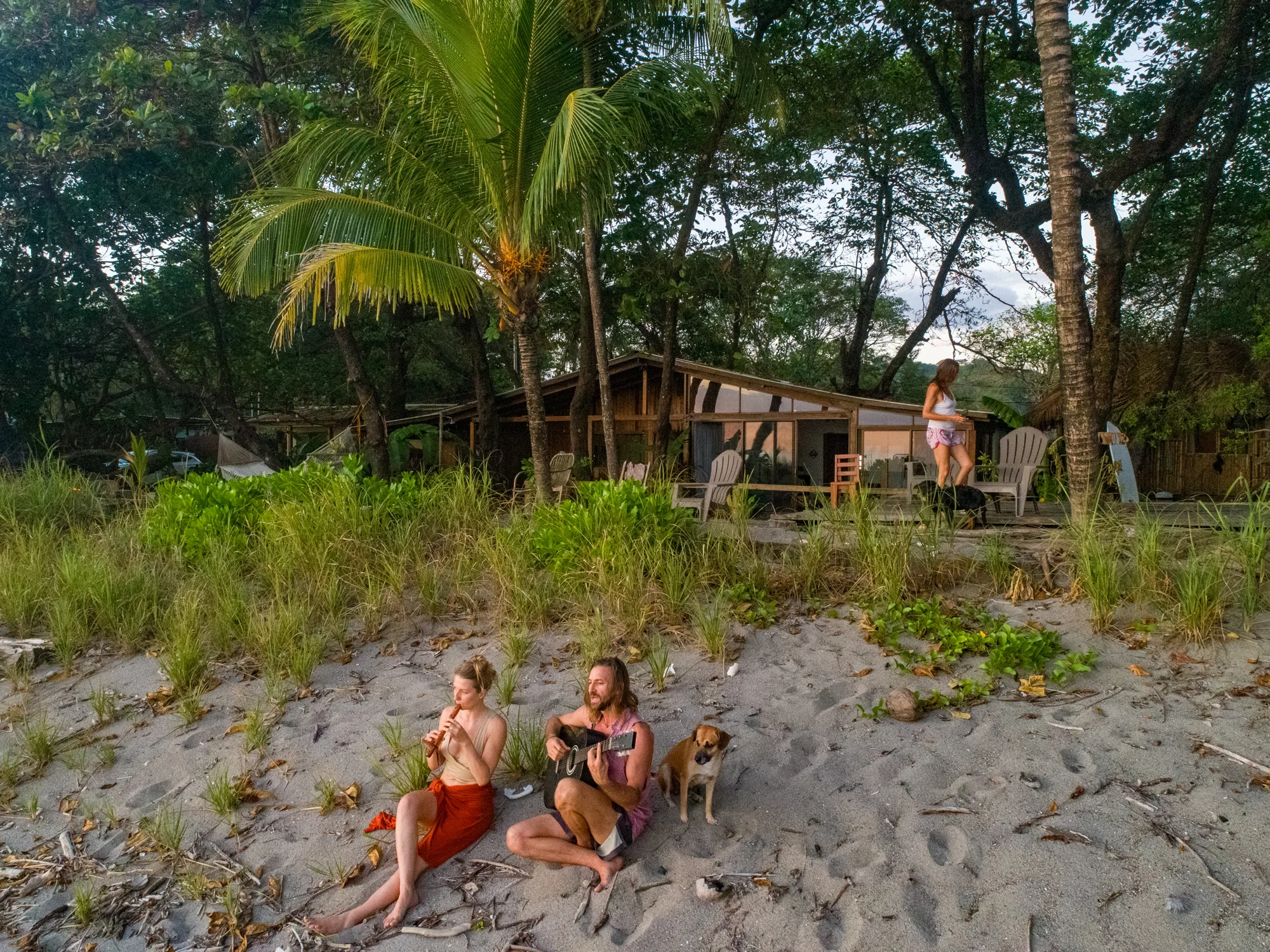 Two people playing music on the beach in front of House of Waves
