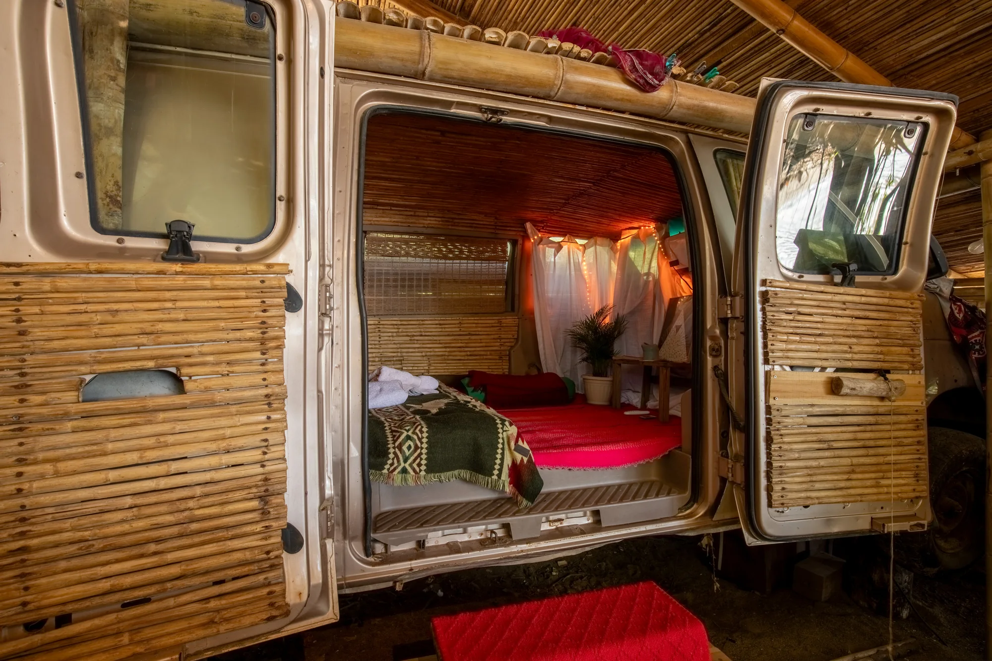 Open side door of the bamboo-clad van revealing its sleeping space